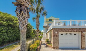 A two-story house with a brick garage, a balcony, and a pathway lined with plants. - Oceanside Manor – High Tide: Beachside Luxury (Surf City)