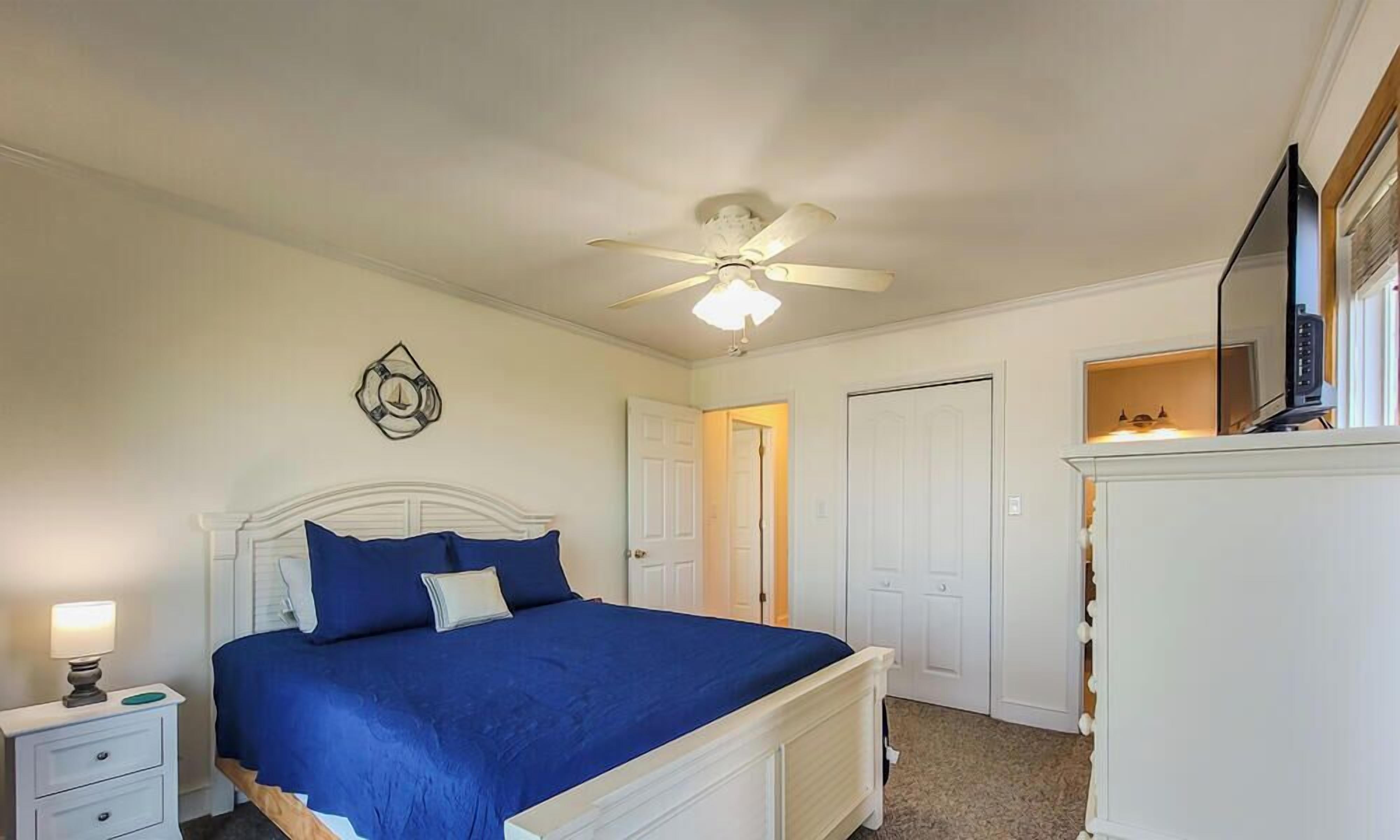 A bedroom with a bed, a nightstand, a dresser, a ceiling fan, and a door.