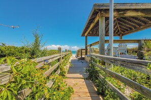 Un paseo marítimo de madera que conduce a una zona de playa con una estructura cubierta y sillas.