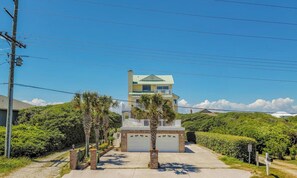 A two-story house with a garage, surrounded by greenery and a clear sky.