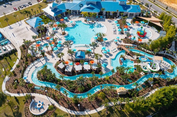 Relax by the central pool surrounded by palm trees and lounge chairs, with multiple water slides and a wave pool nearby.