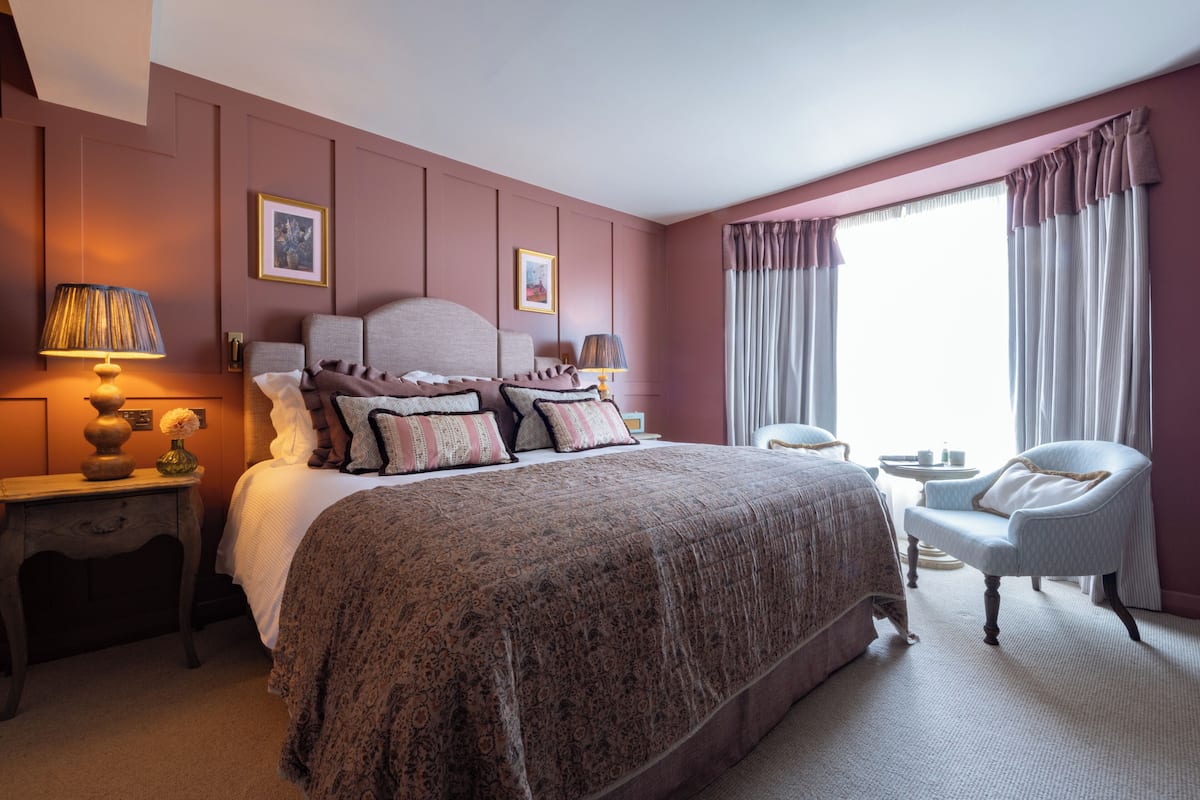 A bedroom with a large bed, two bedside tables, a chair, and a window with curtains.