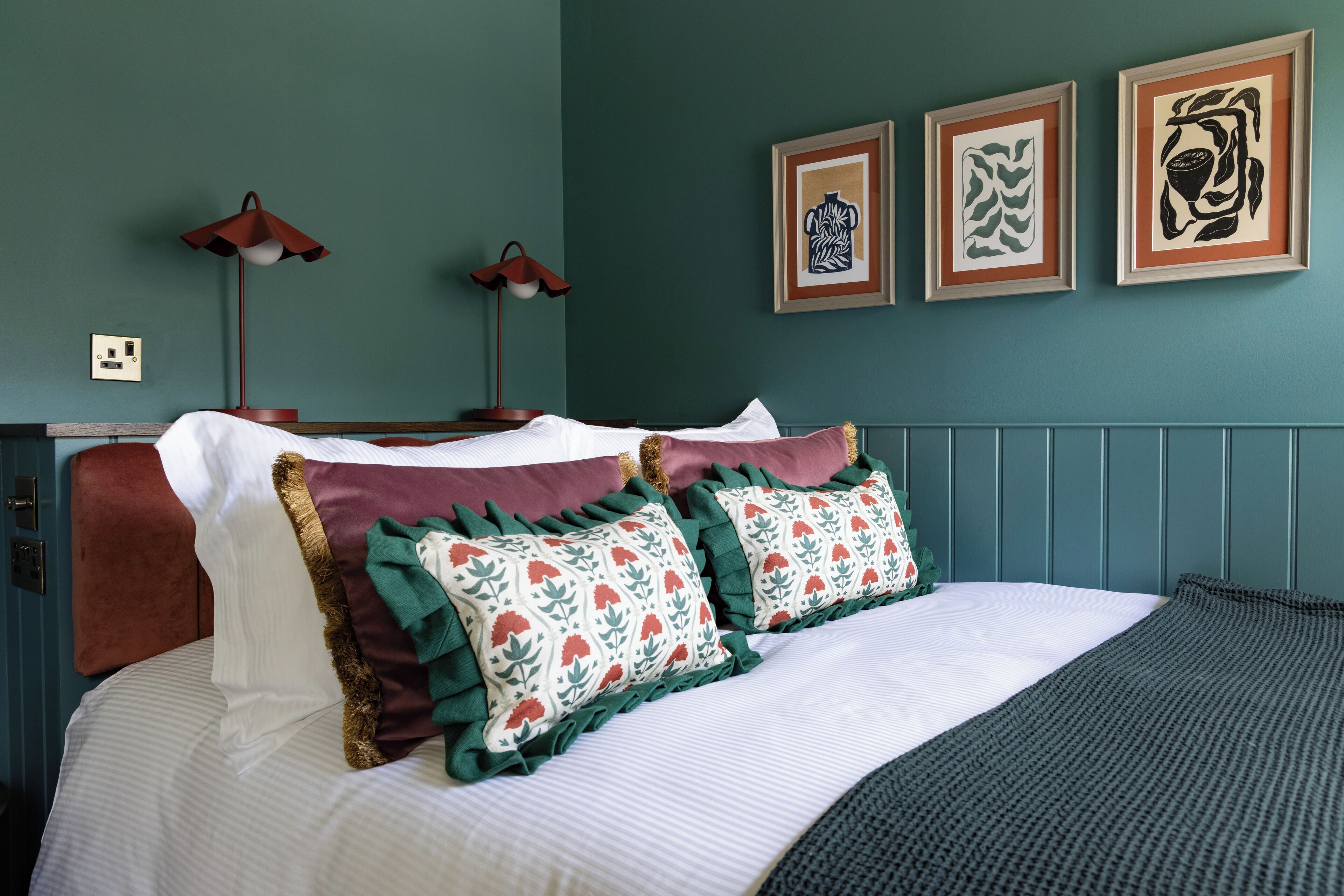 A neatly made bed with decorative pillows, two bedside lamps, and framed artwork on the wall.