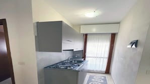 A compact kitchen with a gas stove, cabinets, and a window with curtains. - Great Flat in a Residence With Pool in Rosolina (Rosolina)