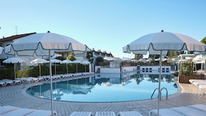 A pool area with lounge chairs and umbrellas, surrounded by buildings. - Great Flat in a Residence With Pool in Rosolina (Rosolina)