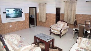 A spacious living room with a television, a chandelier, and a dining area with a table and chairs. - Castle Majestic Hotel  (Enugu)