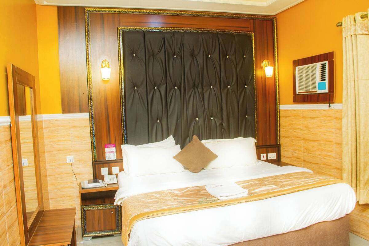 Een hotelkamer met een groot bed, een houten hoofdbord, een nachtkastje met een telefoon en een wandgemonteerde airconditioning.