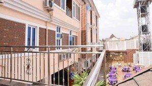 A multi-story building with balconies, a rooftop terrace with purple umbrellas, and a water tower in the background. - Castle Majestic Hotel  (Enugu)