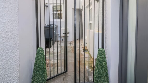 A gated courtyard with a white wall, a metal gate, and a small green plant. - Hocking Cottage (Torquay)