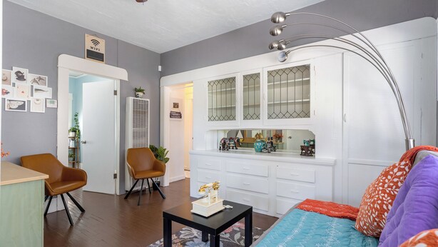 Una sala de estar con sofá, sillas, una mesita de centro y una zona de cocina con armarios y una ventana.