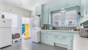 Una cocina con armarios azul claro, un refrigerador blanco y una ventana con persianas.