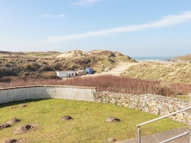 Un paisaje costero con un pequeño edificio, un muro de piedra y una zona cubierta de hierba.