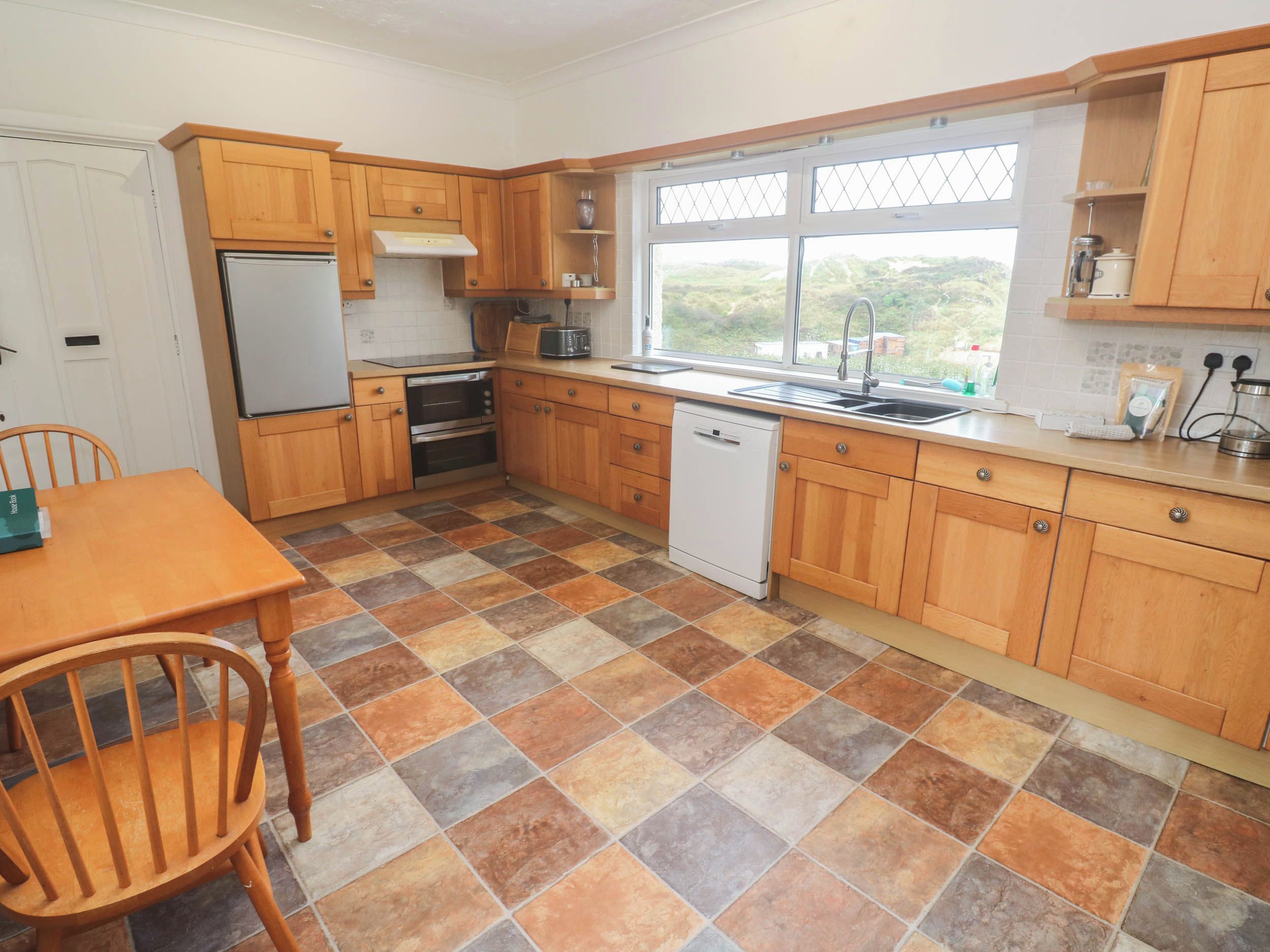 A compact kitchen with wooden cabinets, a dishwasher, a microwave, and a window with a view.