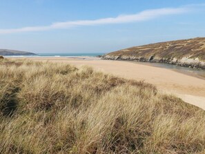 A coastal landscape with a sandy beach, grassy dunes, and a clear view of the sea. - 1 Atlantic View (Newquay)