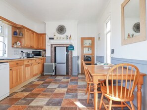 A kitchen with wooden cabinets, a tiled floor, a refrigerator, and a dining table with chairs. - 1 Atlantic View (Newquay)