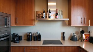 A modern kitchen with wooden cabinets, a built-in oven, a coffee machine, and a kettle on the countertop.
