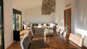 A spacious dining area with a large wooden table, comfortable seating, and a decorative hanging light fixture.
