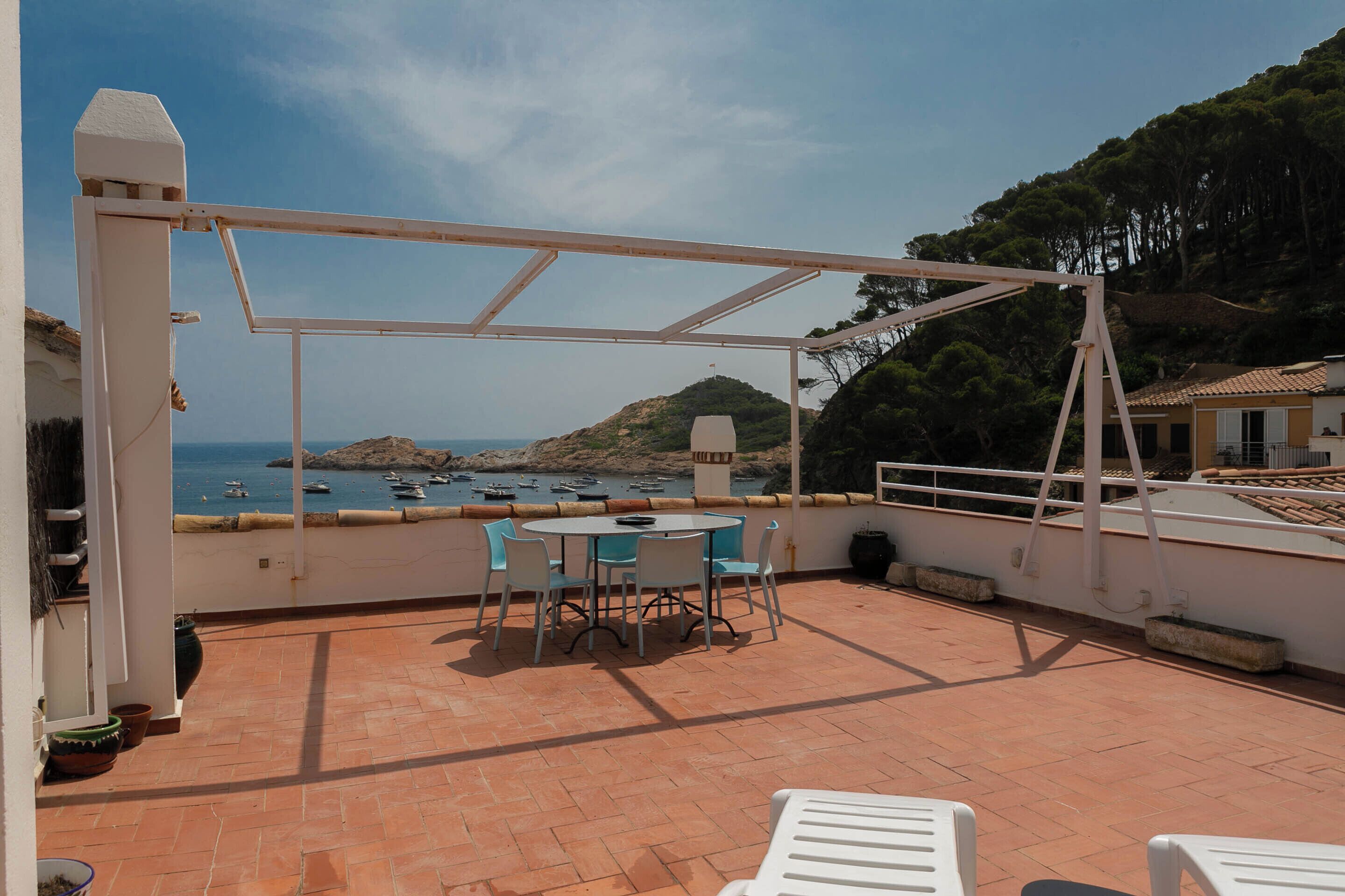 Una terraza con mesa y sillas, con vistas a una zona costera con barcos y colinas.