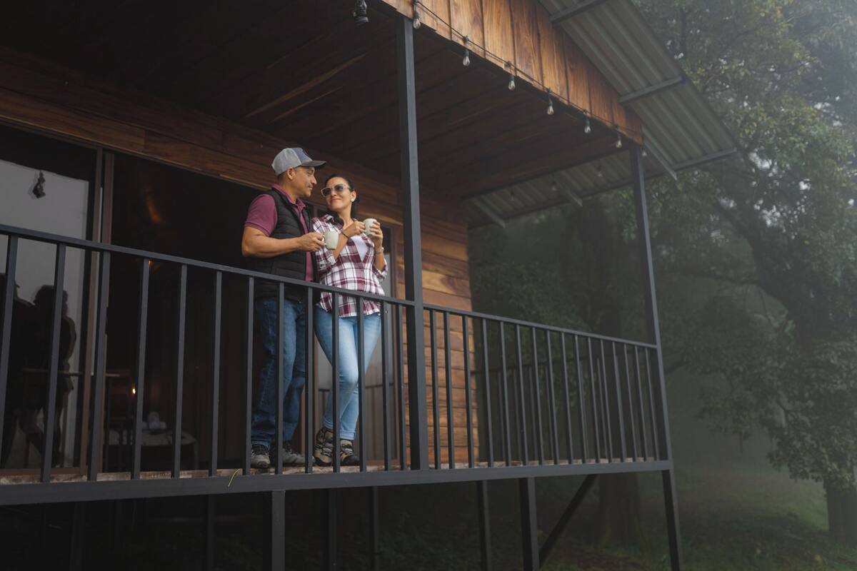 Un balcon en bois avec des rampes en métal, donnant sur une zone boisée.