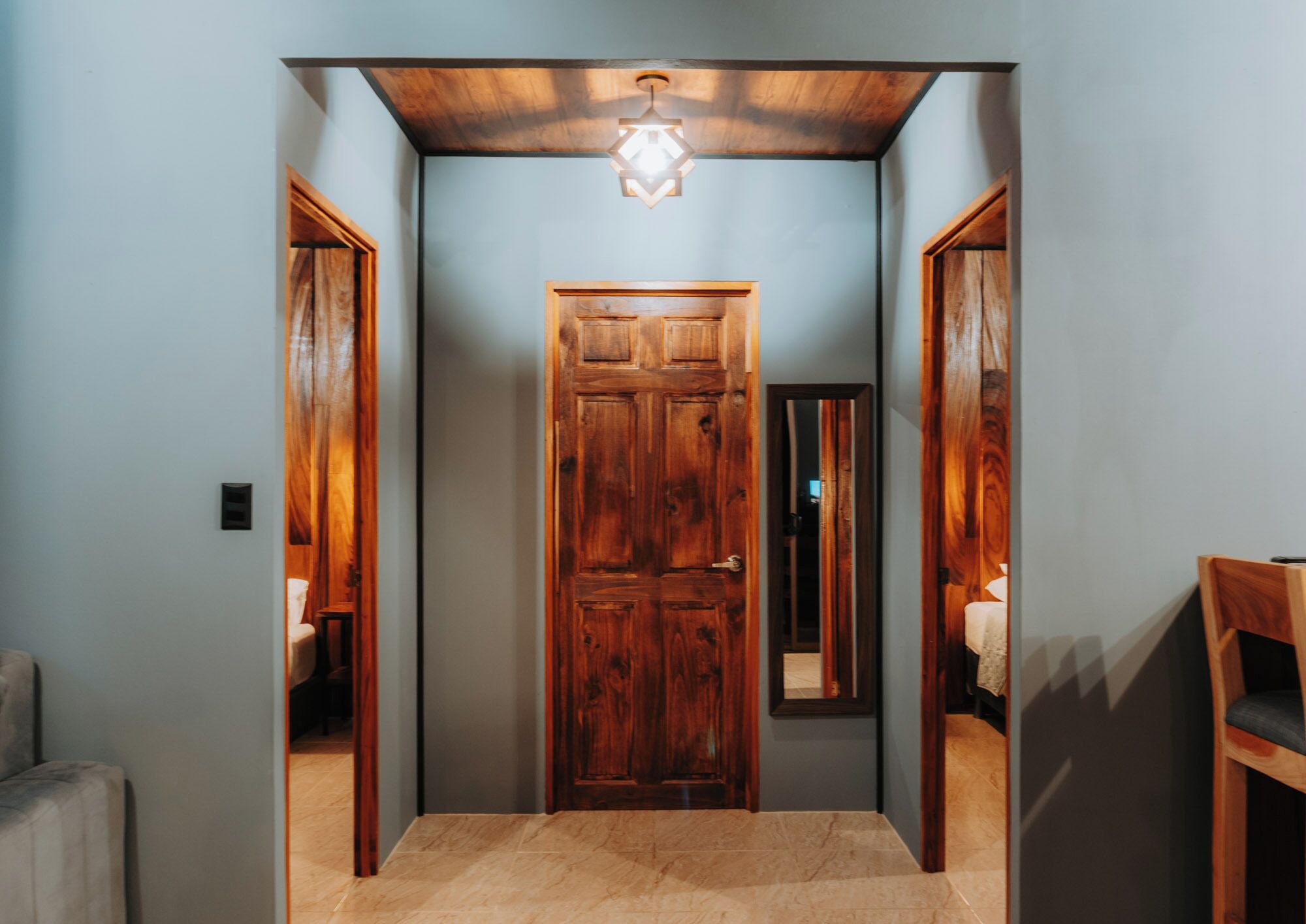 A hallway with a wooden door, a mirror, and a light fixture.