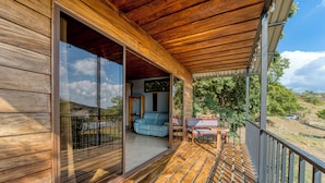Una terraza de madera con un ventanal corredera que da a una habitación con sofá y una mesa.