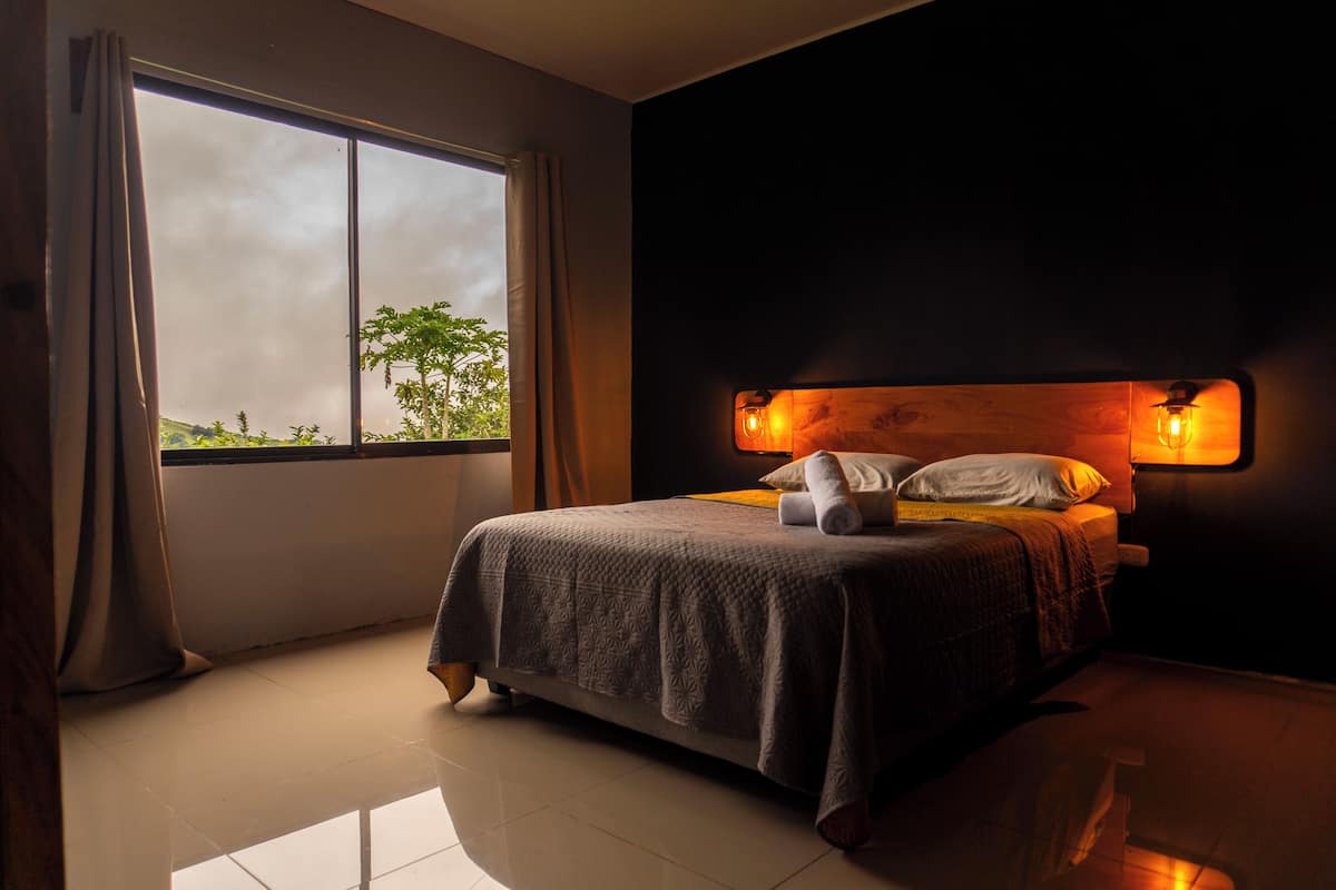 Une chambre avec une grande fenêtre, un lit avec une tête de lit et une table de chevet.