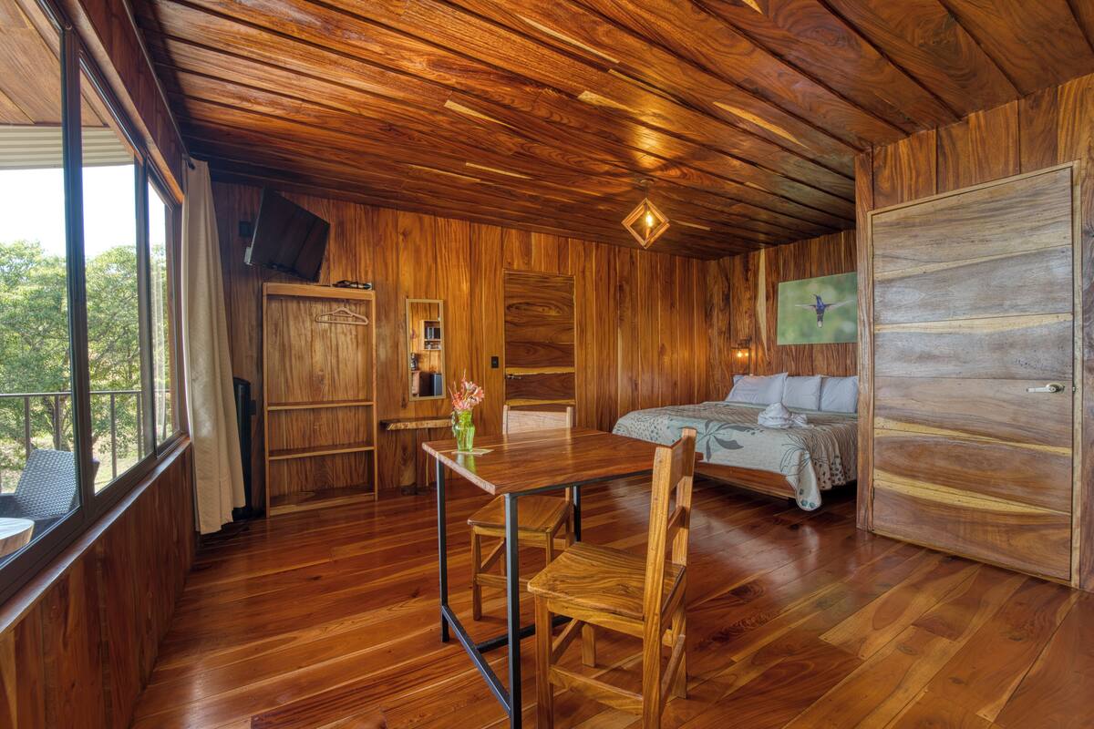 Un intérieur en bois comprenant un lit, une table à manger avec des chaises, un téléviseur et une fenêtre.