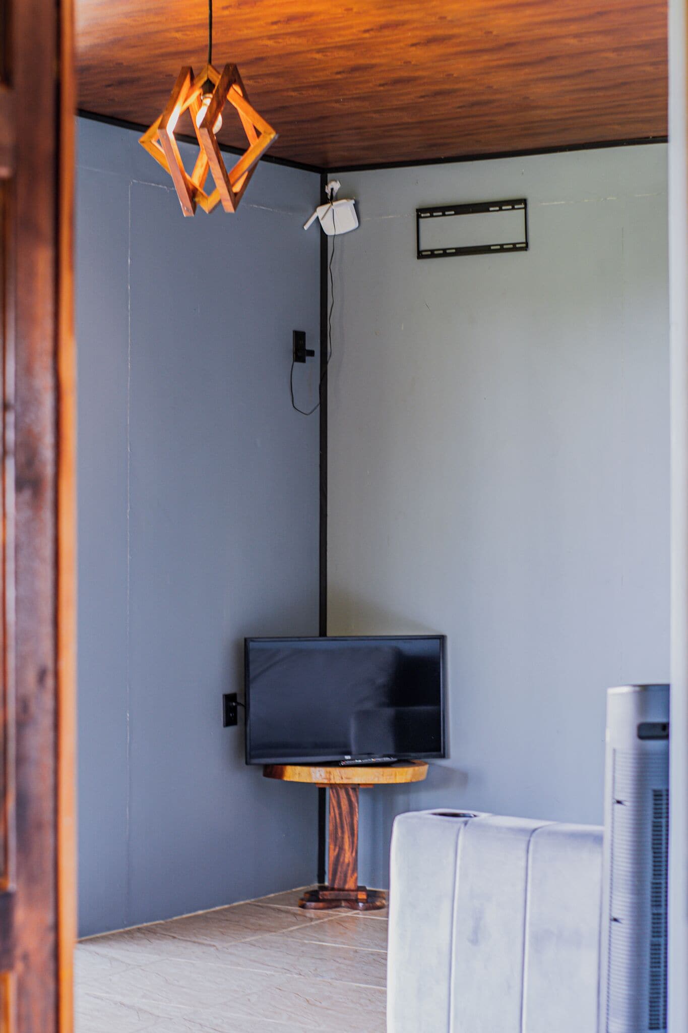 Una habitación con televisión sobre un soporte de madera, una lámpara en el techo y un equipo de aire acondicionado.