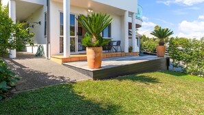Une maison moderne à deux étages, dotée d’un patio couvert, de grandes fenêtres et de plantes en pot.