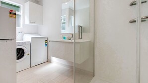 Une cuisine moderne équipée d’un lave-linge, d’un réfrigérateur et d’une cabine de douche en verre.