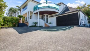 Une maison moderne à deux étages, dotée d’un balcon incurvé, d’un garage et d’une allée menant à la maison, avec un symbole vert représentant un vélo.