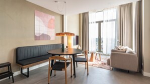 Ein modernes Wohnzimmer mit einer Couch, einem runden Esstisch, zwei Stühlen, einer Bank und einem großen Fenster mit Vorhängen.