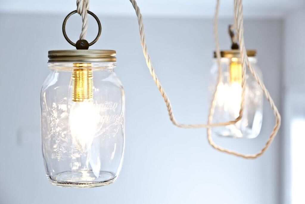 Two hanging light bulbs in clear glass jars with metal lids and twisted rope.