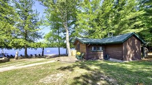 Eine Blockhütte mit einer Terrasse, umgeben von Bäumen und einem See.