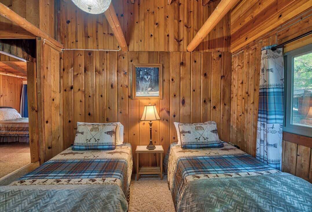 Une chambre rustique en bois avec deux lits, un tableau encadré au mur et une fenêtre avec des rideaux.