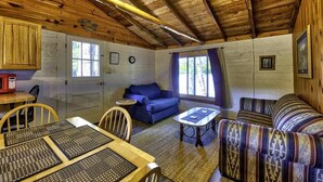 Ein rustikales Cabin-Interieur mit Esstisch, blauer Couch, gemustertem Sofa und Decke mit freiliegenden Balken.