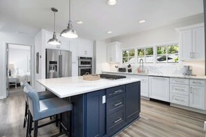A modern kitchen with white cabinets, stainless steel appliances, and a central island with bar stools.