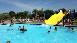 A swimming pool with a yellow slide and people swimming and playing. - Holiday Home Near Petten Beach With Pool (Petten)
