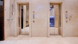 Un ascensor moderno con detalles metálicos y panel de vidrio, flanqueado por paredes y suelo de mármol.