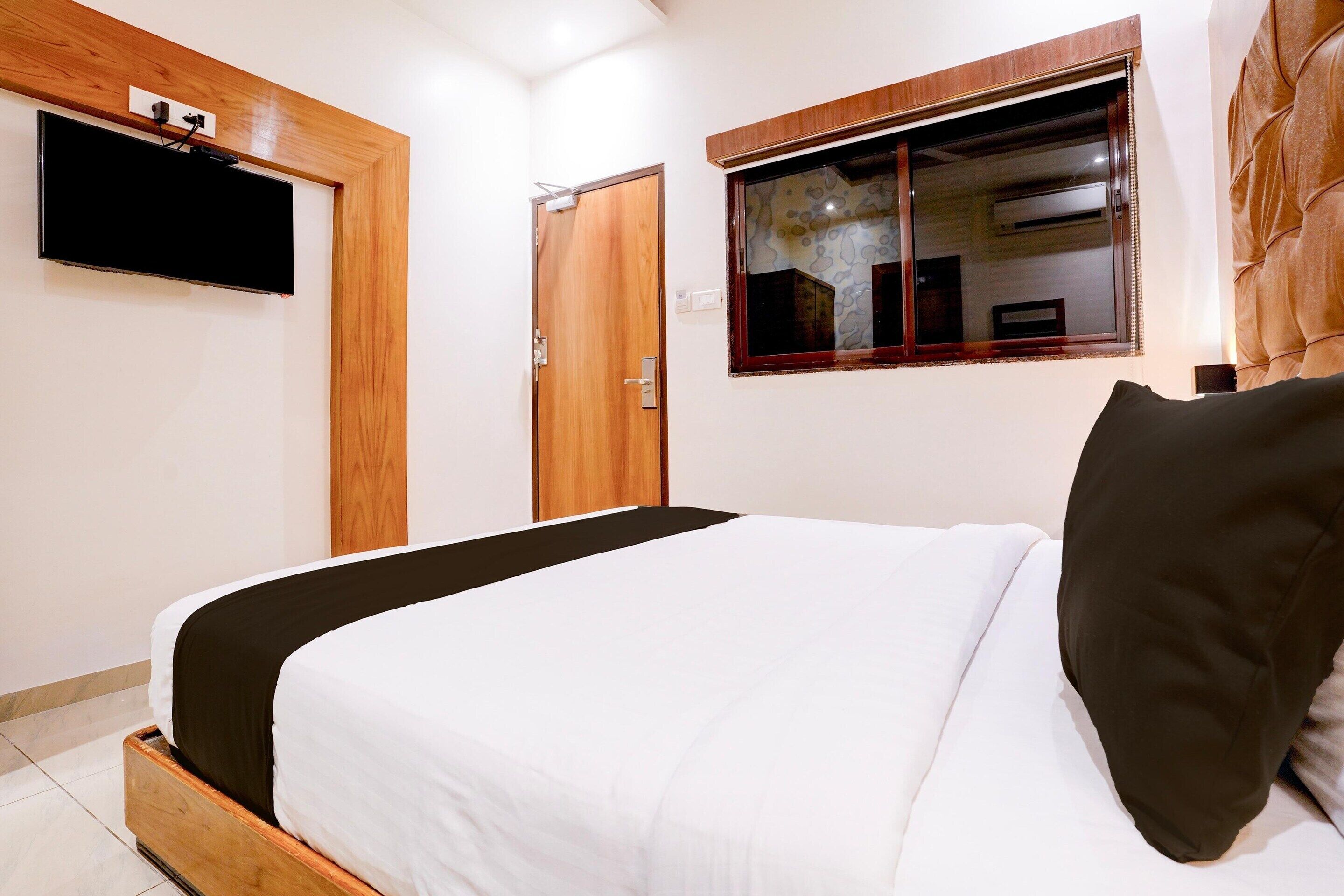 A bedroom with a bed, a TV mounted on the wall, a window with a view, and a door.