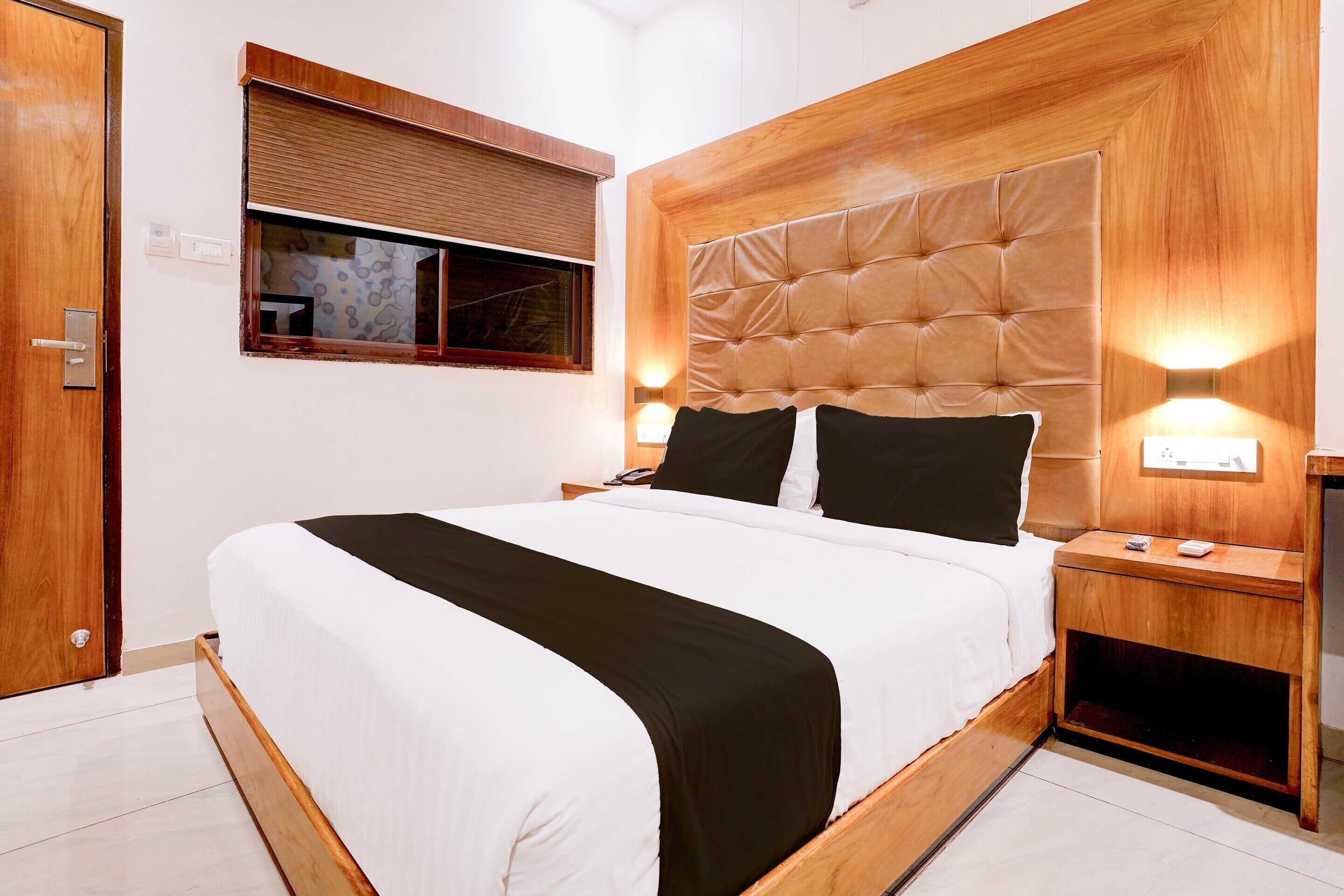 A neatly made bed with a wooden headboard, two bedside tables with lamps, and a window with blinds.