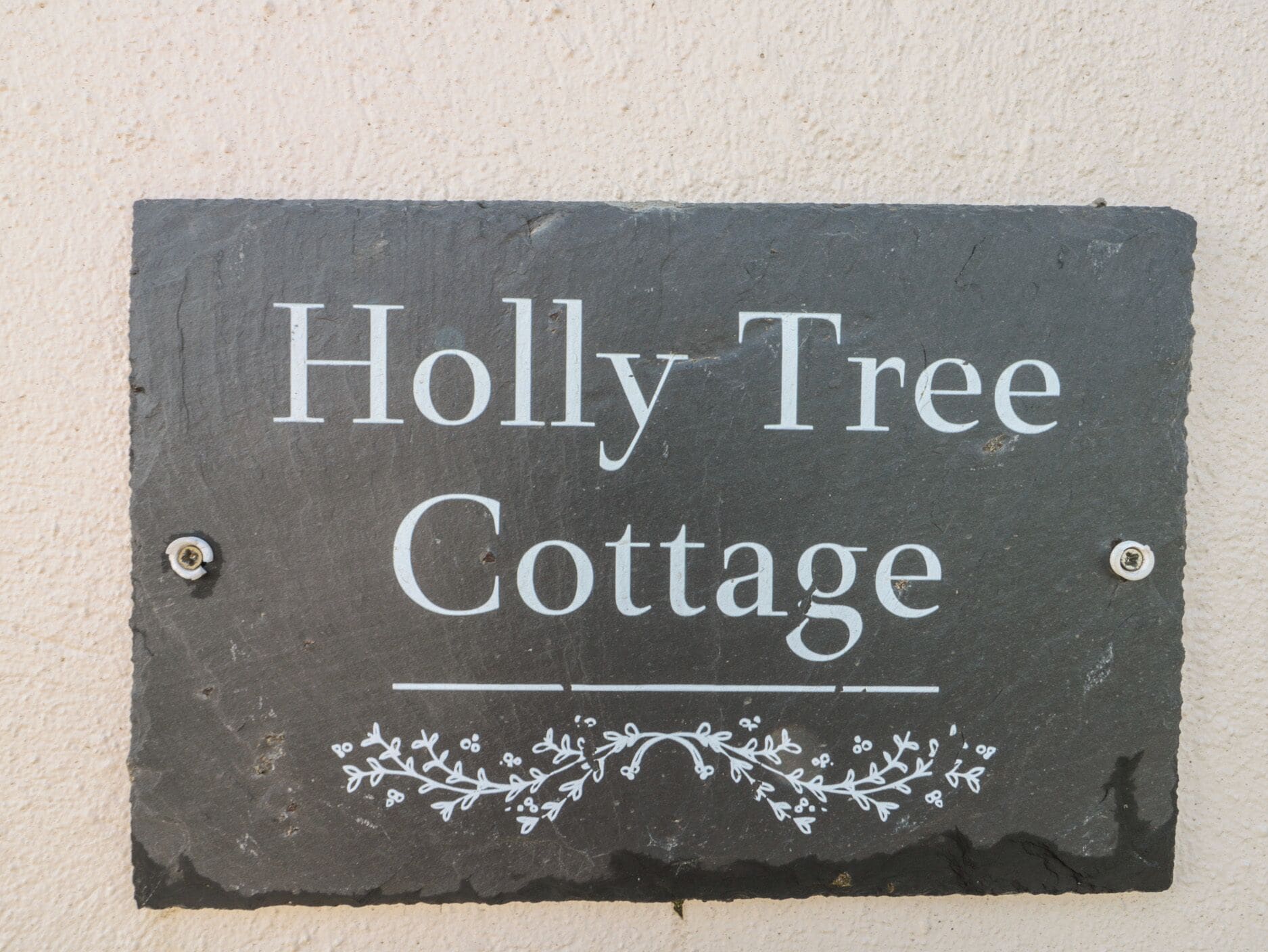 Un letrero de pizarra con la inscripción 'Holly Tree Cottage', adornado con un motivo floral decorativo debajo del texto.