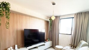 A modern living room with a large flat-screen TV, a beige sofa, and a small side table. - Cayenne By Day by Day (Joao Pessoa)