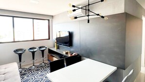 A modern kitchen with a dining area, a sofa, and a TV on the wall. - Cayenne By Day by Day (Joao Pessoa)