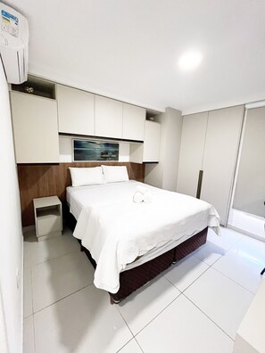 Een hotelkamer met een bed, een klein nachtkastje, een ingebouwde televisie en een kledingkast.