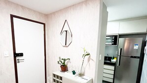 A modern kitchen with a built-in oven and refrigerator, a white cabinet with a plant, and a door with a handle. - Cayenne By Day by Day (Joao Pessoa)