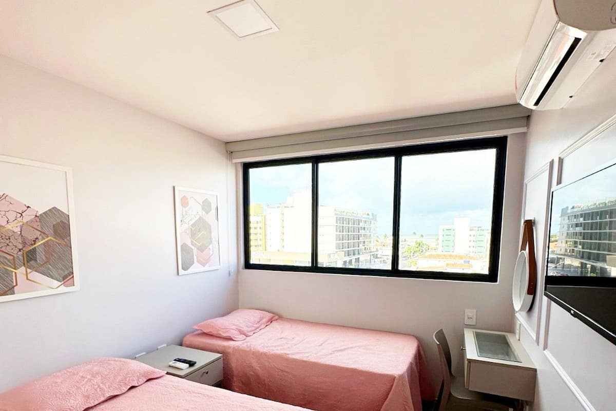 Une chambre avec deux lits, un bureau, une chaise et une fenêtre donnant sur la ville.