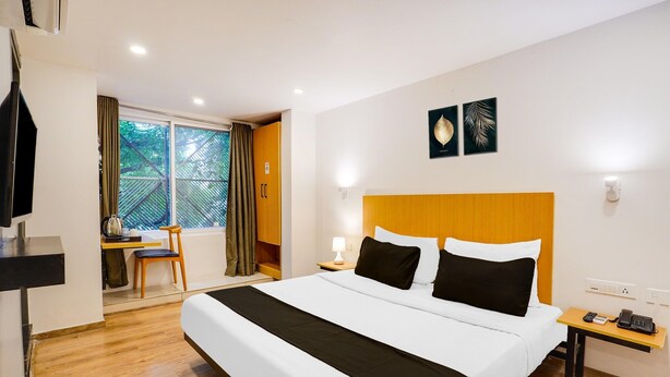 Une chambre d’hôtel avec un grand lit, un bureau avec une chaise, une fenêtre avec des rideaux et un téléphone fixé au mur.