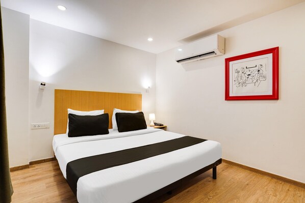 A hotel room with a bed, bedside table, lamp, and a framed picture on the wall.
