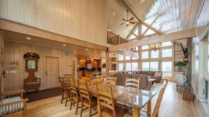 A spacious dining area with a long wooden table and chairs, a kitchen in the background, and a balcony with a view.